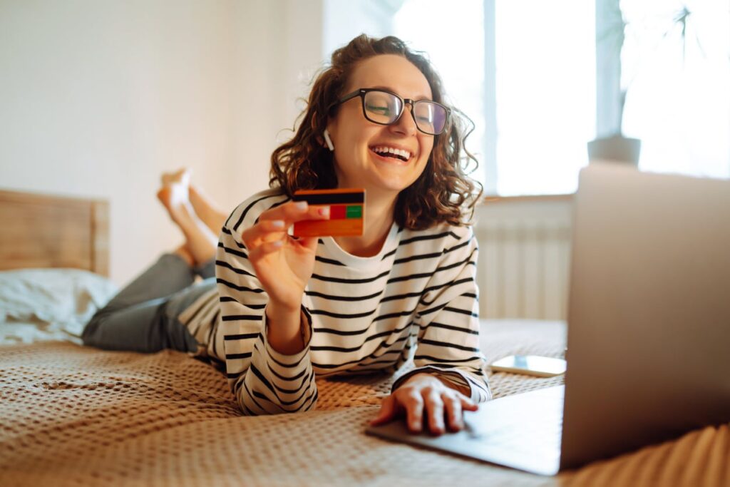 jeune femme en train de faire du shopping en ligne avec sa carte bancaire à la main